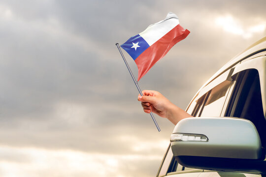 Waving the Chile flag against the sunrise or sunset from a car driving along a country road. Holding the Chile flag, traveling by car, on a weekend trip.