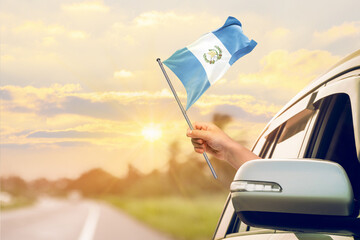 Waving the Guatemala flag against the sunrise or sunset from a car driving along a country road....