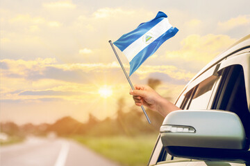 Waving the Nicaragua flag against the sunrise or sunset from a car driving along a country road. Holding the Nicaragua flag, traveling by car, on a weekend trip.