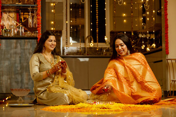 Smiling Women Celebrating Diwali with Rangoli and Diyas,Women decorating Home on the festival occasion with diya and flowers