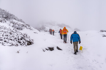Group of hikers trekking through a snowy mountain trail in foggy conditions, wearing colorful winter gear. Adventurous winter expedition in a remote, cold landscape.

