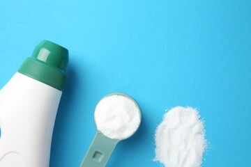 Bottle of laundry detergent and measuring scoop of washing powder on blue background, flat lay....