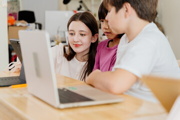 Young teacher guides diverse students with digital devices in modern classroom. Multiethnic elementary school setting - technology in education.