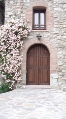 Fototapeta premium A charming rose bush with pink flowers cascades over a weathered stone wall, framing a small window and door in a peaceful setting in France