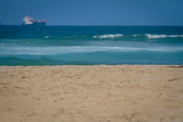 An empty scene looking out at sand and ocean waves and a ship on sunny day with a clear blue sky