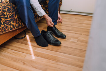A man is getting ready to put on his shoes. He is sitting on a bed and has a pair of socks on