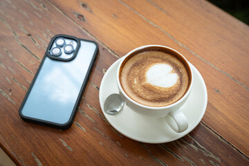 Hot coffee latte with latte art milk foam in cup mug,smartphone on wood desk on top view. As breakfast In a coffee shop at the cafe,during business work concept,vintage style