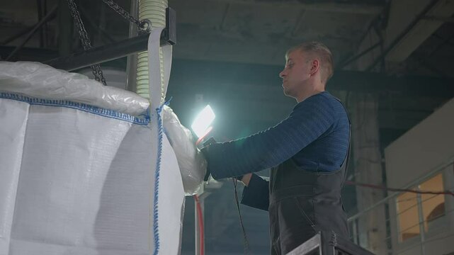 Worker controlling automated equipment at the plastic compounding factory. Worker presses buttons on device at a plastic compounding plant. Industrial worker looks inside the plastic compounding bag.