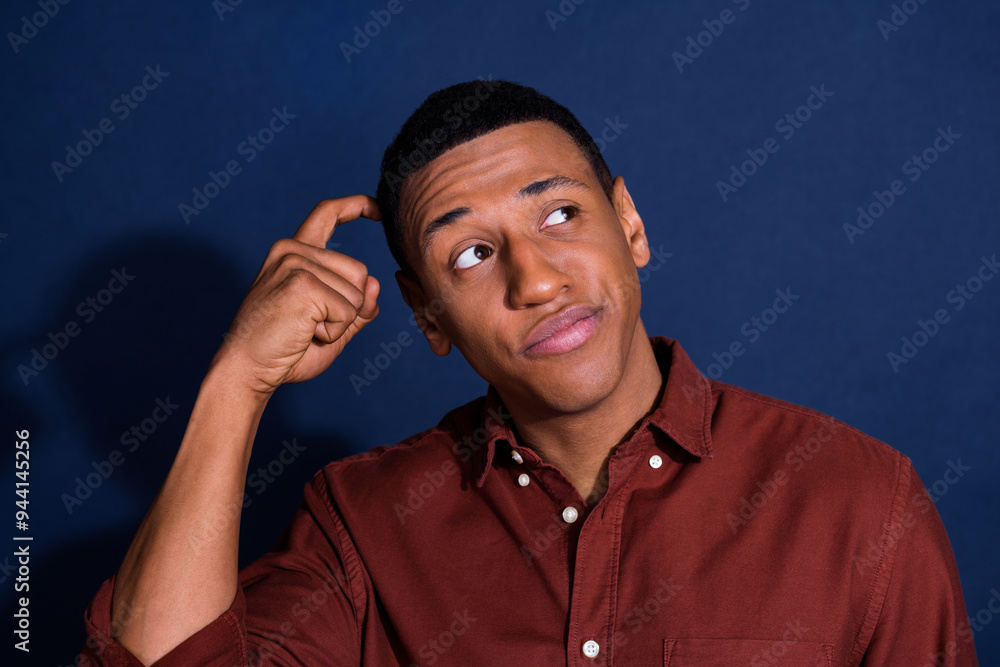 Wall mural Photo of young man scratch head look empty space wear brown shirt isolated on dark blue color background