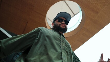 Motion shot of asian handsome hipster pose in hip hop style while looking at camera. Low angle image of professional street dancer dance in freestyle movement at mall. Outdoor sport 2024. Hiphop.