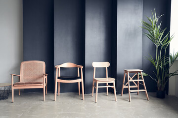 Wooden chairs of different shapes and designs, arranged in a row, are waiting for visitors. On a black uneven wall in black with space to copy. High quality photo