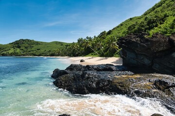 Obraz premium Waves hitting a rock on a picture-perfect, sandy beach on the Yasawa Islands in Fiji. White sand, turquoise water, and Palm trees. Tropical island paradise near the main island of Fiji. 