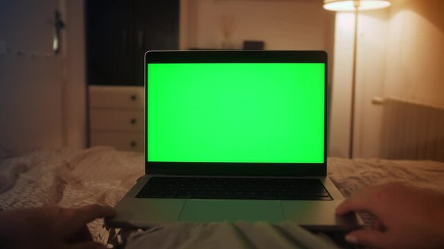 Woman uses a laptop with green screen lying on the couch in an apartment. Close-up of the screen, an unrecognizable person.