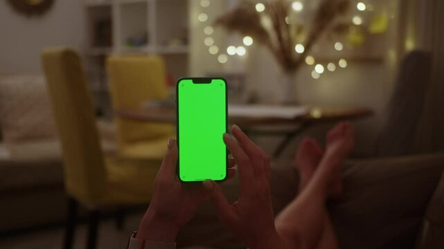 Casual lifestyle and leisure on comfortable sofa at living room. Woman relaxing after work at night using smartphone. Phone with green screen chroma key for copy space.