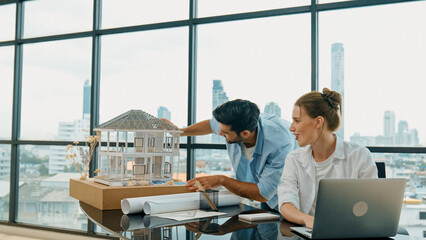 Smart architect engineer inspect house model while colleague using laptop analysis data. Professional designer team working together to design house model construction at modern office. Tracery