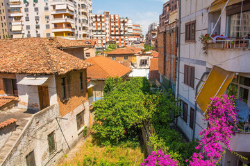 Housing with old and new contrasting architectural styles in the centre of Tirana, central Albania. In the centre is an overgrown courtyard with bougainvillea flowers