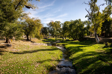 Tranquil stream of water across Alta Gracia town surrounded by grass and trees with horse grazing in autumn