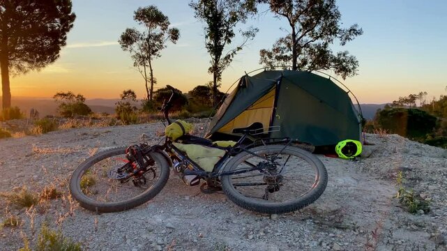 Golden sunset light illuminating a bikepacking mountain bike and tent camping on a mountain top in Andalusia, Spain.