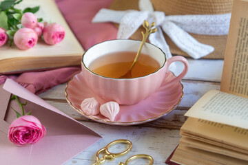 A cup of aromatic tea, a book and a rose on the table.