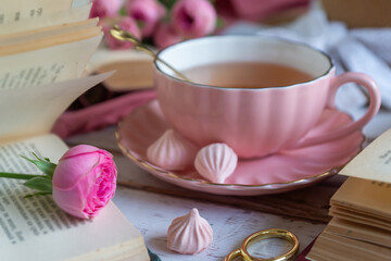 A cup of aromatic tea, a book and a rose on the table.