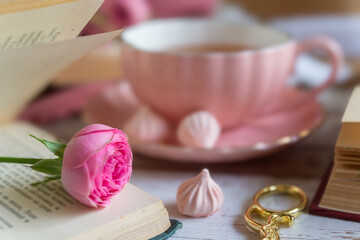 A cup of aromatic tea, a book and a rose on the table.