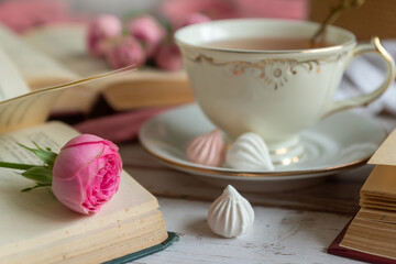 A cup of aromatic tea, a book and a rose on the table.