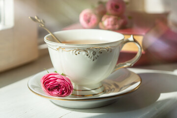 A cup of aromatic tea, a book and a rose on the table.