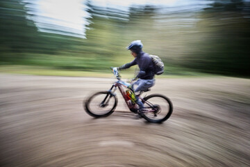 Fototapeta premium Motion blur. Cyclist man riding electric mountain bike outdoors. Male tourist biking along trail in the forest. Concept of sport, active leisure and nature.