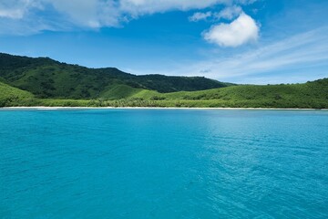 Picture-perfect image of the turquoise ocean in front of deep lush hills of a small island covered by coconut palm trees. Paradise-like island beach scene. Yasawa Islands of Fiji. Travel Destination. 