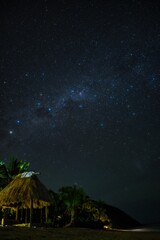Fiji nighttime beach scene on a small island. Stunning night sky and Milky Way over the Yasawa Islands, Fiji. Palm trees, stars, and the beach in the night. Small hut underneath the stars. 