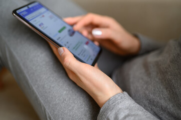 Woman sitting on sofa at home, looking at information about cars on mobile phone, close-up. Girl...