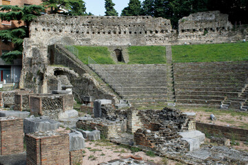 Dilapidated stone roman amphitheatre with rocks and grass.