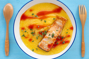 Bowl with polenta, grilled salmon, tomato sauce over wooden background.