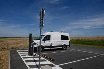An electric van is charging at a charge station in the middle of the fields and in the middle of nowhere.