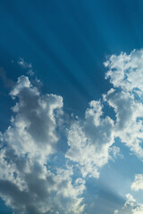 The sun's rays, passing through the contours of white dense fluffy clouds, leave clear traces in the blue sky at an oblique angle. Abstract photography that makes you think about the world