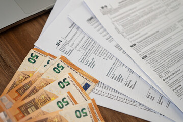 Tax forms and fifty-euro banknotes on a wooden desk. Financial management and international tax preparation concept. Suitable for accounting and finance-related themes 