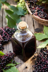 A bottle of black elder syrup with fresh elderberries and leaves