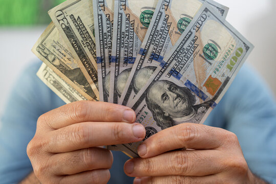 Male financial manager demonstrates dollar banknotes fan after successful currency exchange service with benefiting rate as way to earn extra money sitting in office