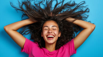 Fototapeta premium Portrait of 20s young woman laughing, wearing pink t-shirt on blue background