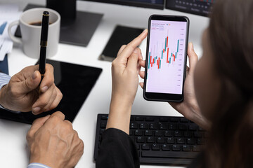 Cropped with focusing on phone with hand pointing with discussing dynamic stock market in two business traders on screens on real time currency rate investment risk data at modern office. Postulate.
