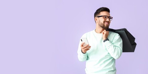 Handsome man with mobile phone and shopping bags on lilac background with space for text