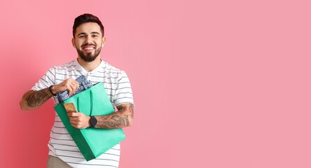 Handsome man with credit card, shopping bag and new clothes on pink background with space for text