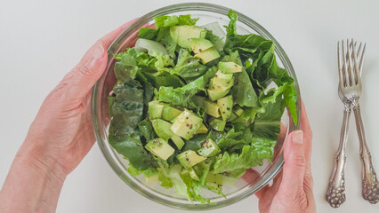 Bowl of fresh green lettuce salad in a woman's hands close-up on white background, view from above
