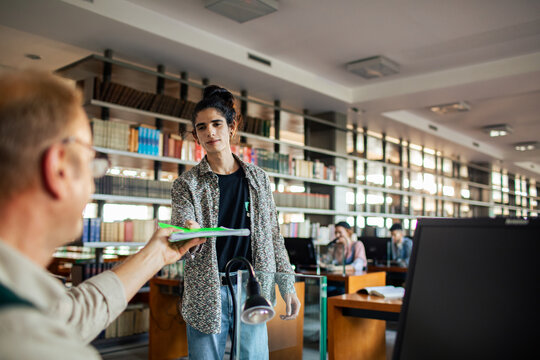 Student submitting paper to professor in college library