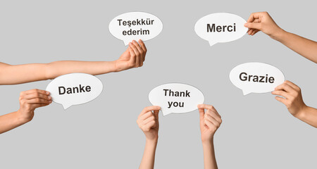 Hands holding speech bubbles with text THANK YOU in different languages on grey background