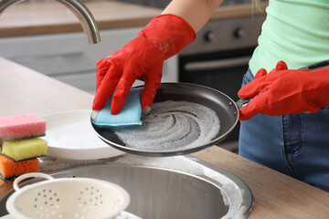 Woman in red rubber gloves washing frying pan with sponge