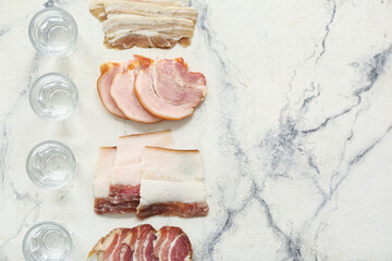 Shots with cold vodka and bacon on white marble background