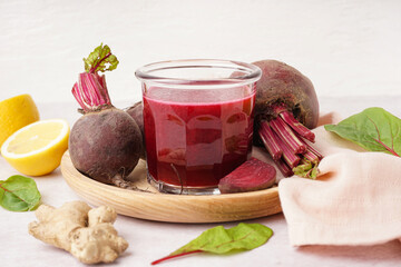 Glass of fresh beetroot juice and vegetables on light background