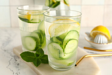 Board and glasses of infused water with cucumber slices on white table