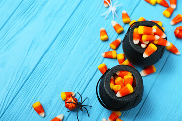 Bowls with tasty Halloween candy corns and spiders on color wooden background, closeup